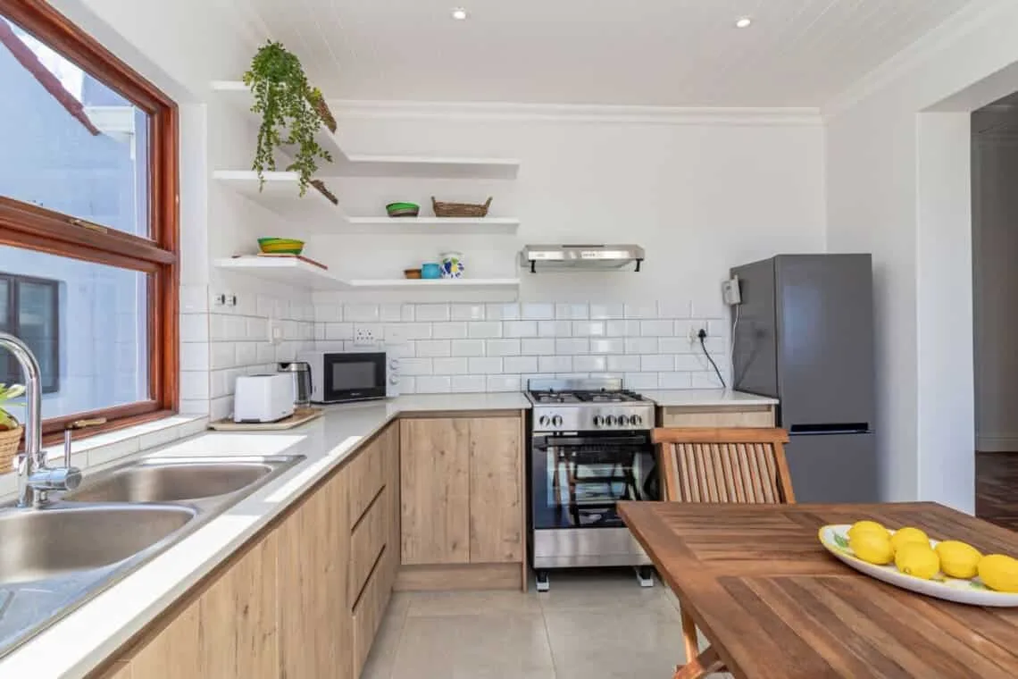 Una cocina luminosa con gabinetes de madera, una estufa de acero inoxidable, un refrigerador y una mesa de comedor de madera.