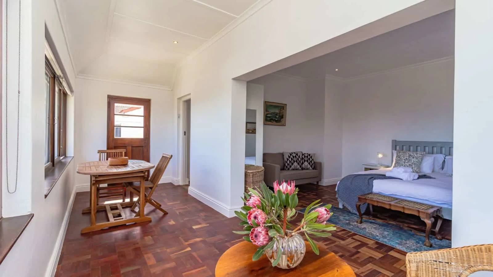 Una estancia luminosa combina una mesa de comedor de madera junto a las ventanas con una cama y una zona de estar.