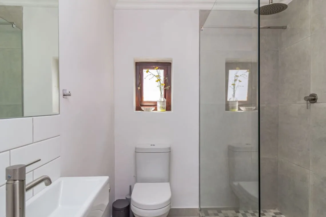 Un baño moderno con lavabo e inodoro blancos junto a una ducha con mampara de vidrio.