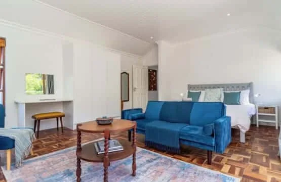 Una luminosa zona de estar en el dormitorio tiene un sofá azul, una cama blanca y una mesa de centro de madera.