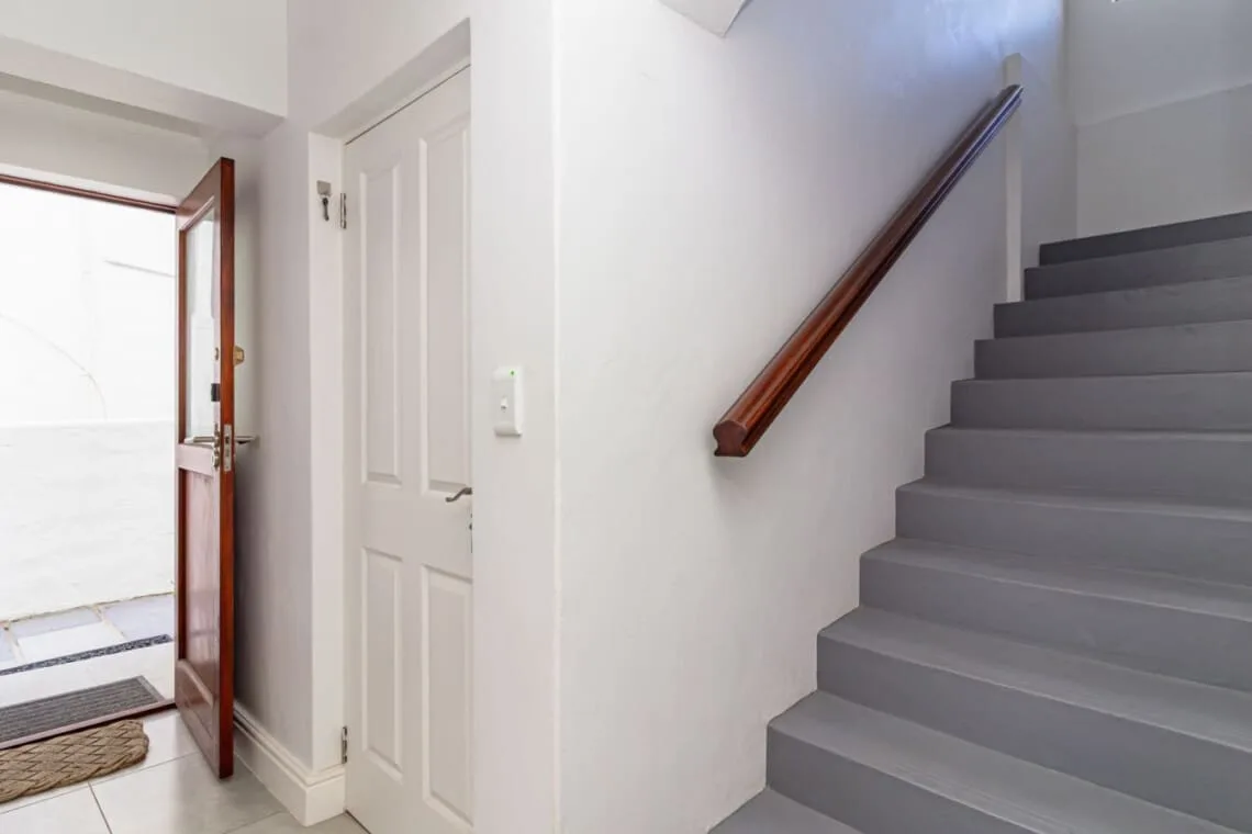 Una escalera interior con peldaños grises y pasamanos de madera junto a una puerta blanca con paneles.