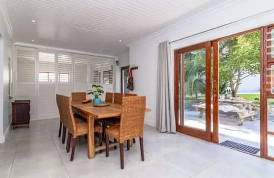 Comedor con mesa de madera y sillas de mimbre junto a grandes puertas de vidrio que dan a un patio.