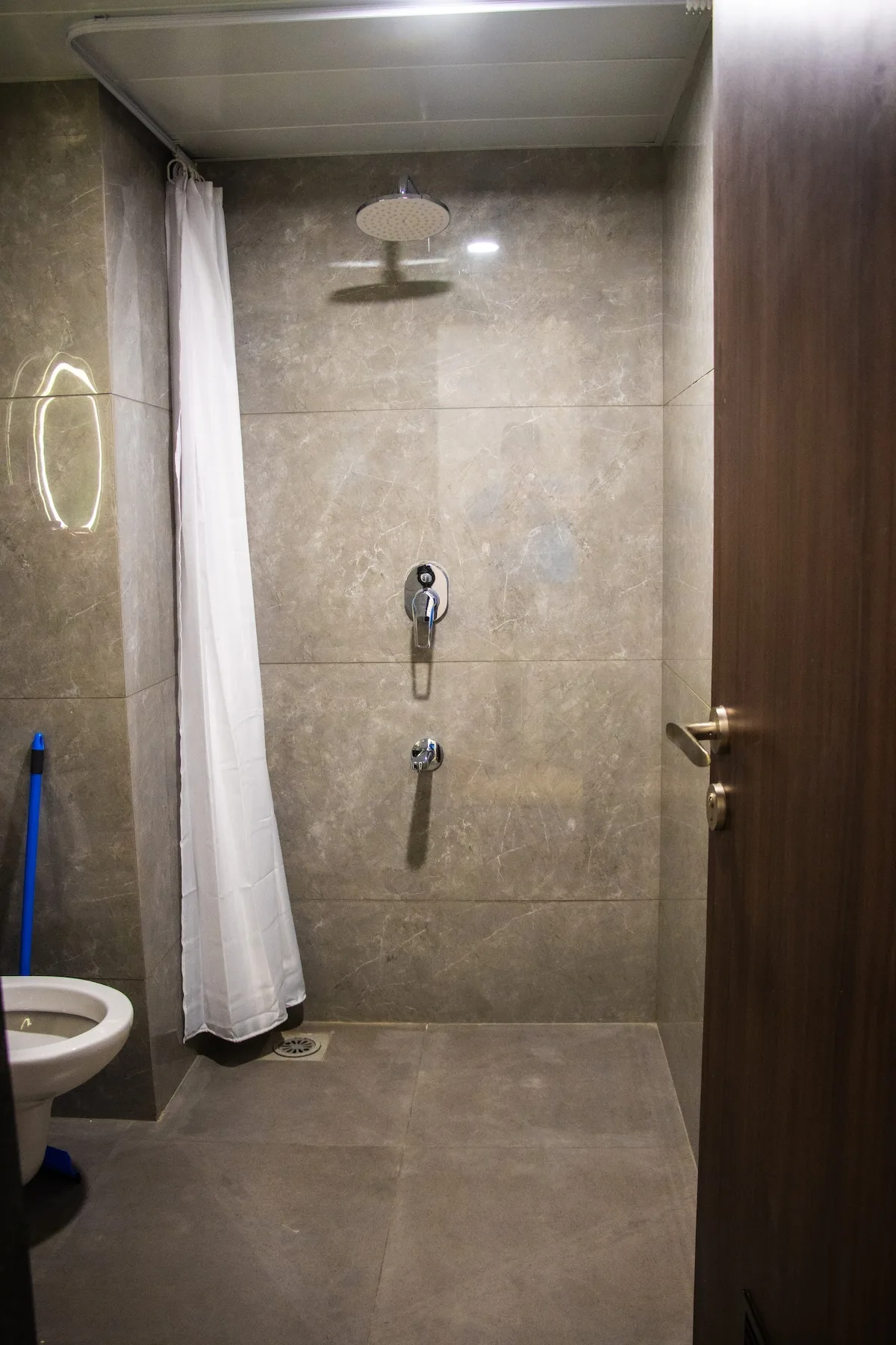 Zona de ducha de baño alicatada, con cortina y rociador montado en la pared.