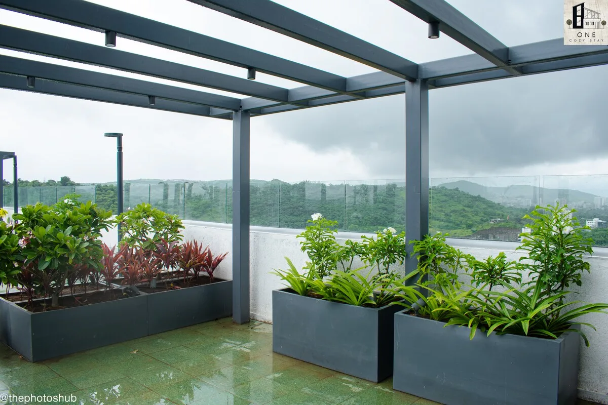 Zona común: Una terraza en la azotea con jardineras elevadas y una barandilla de vidrio da a colinas verdes.