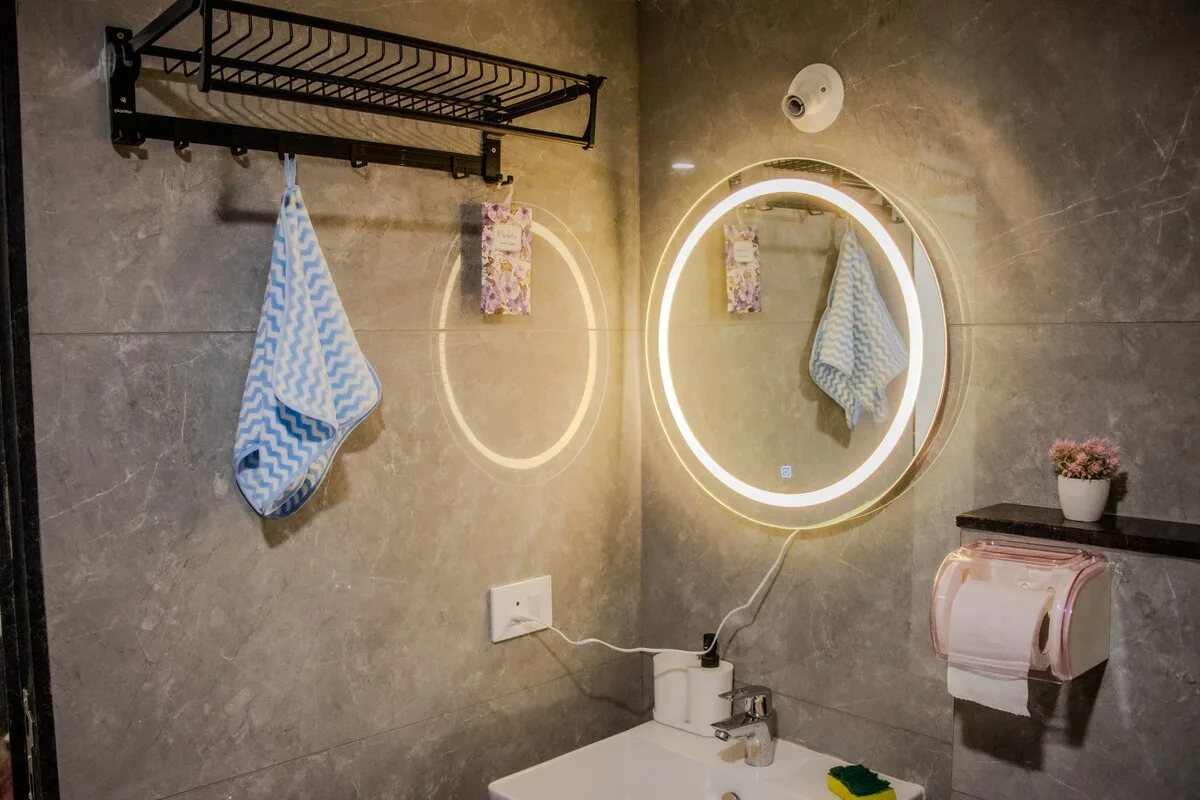 Zona de lavabo con un espejo redondo iluminado y un toallero.