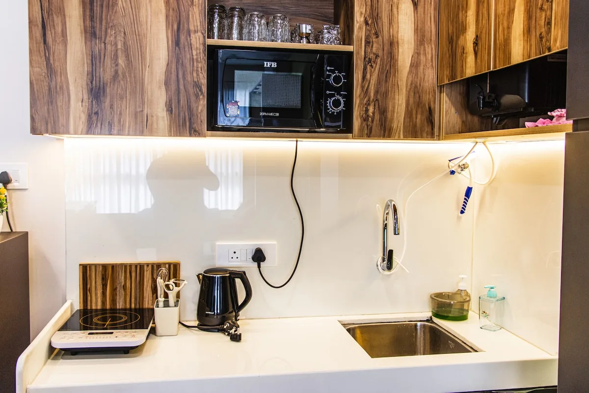 Una encimera de cocina compacta con fregadero, hervidor y microondas bajo armarios de madera.