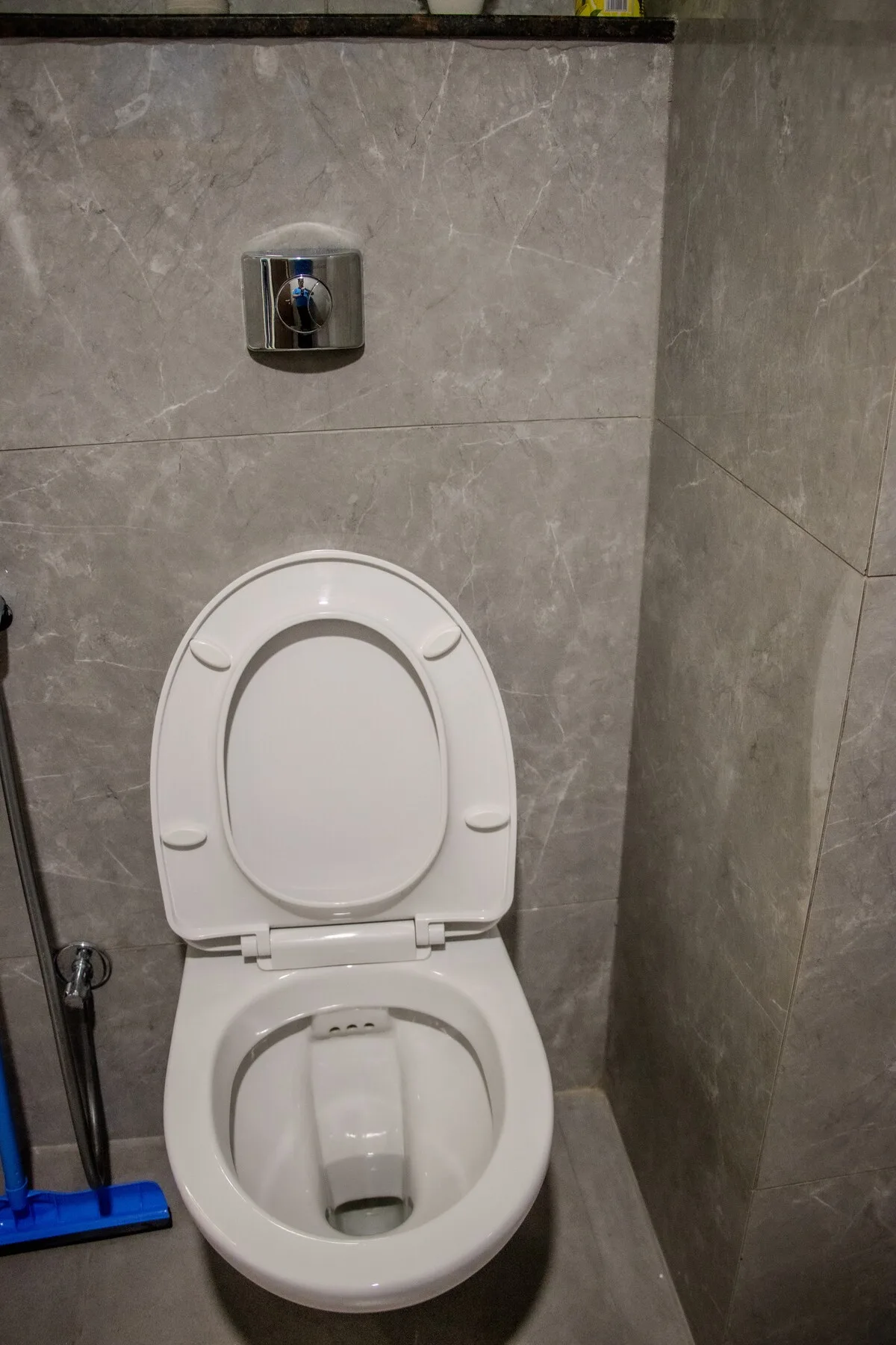 Un inodoro con el asiento levantado está frente a paredes de baño revestidas con azulejos grises.