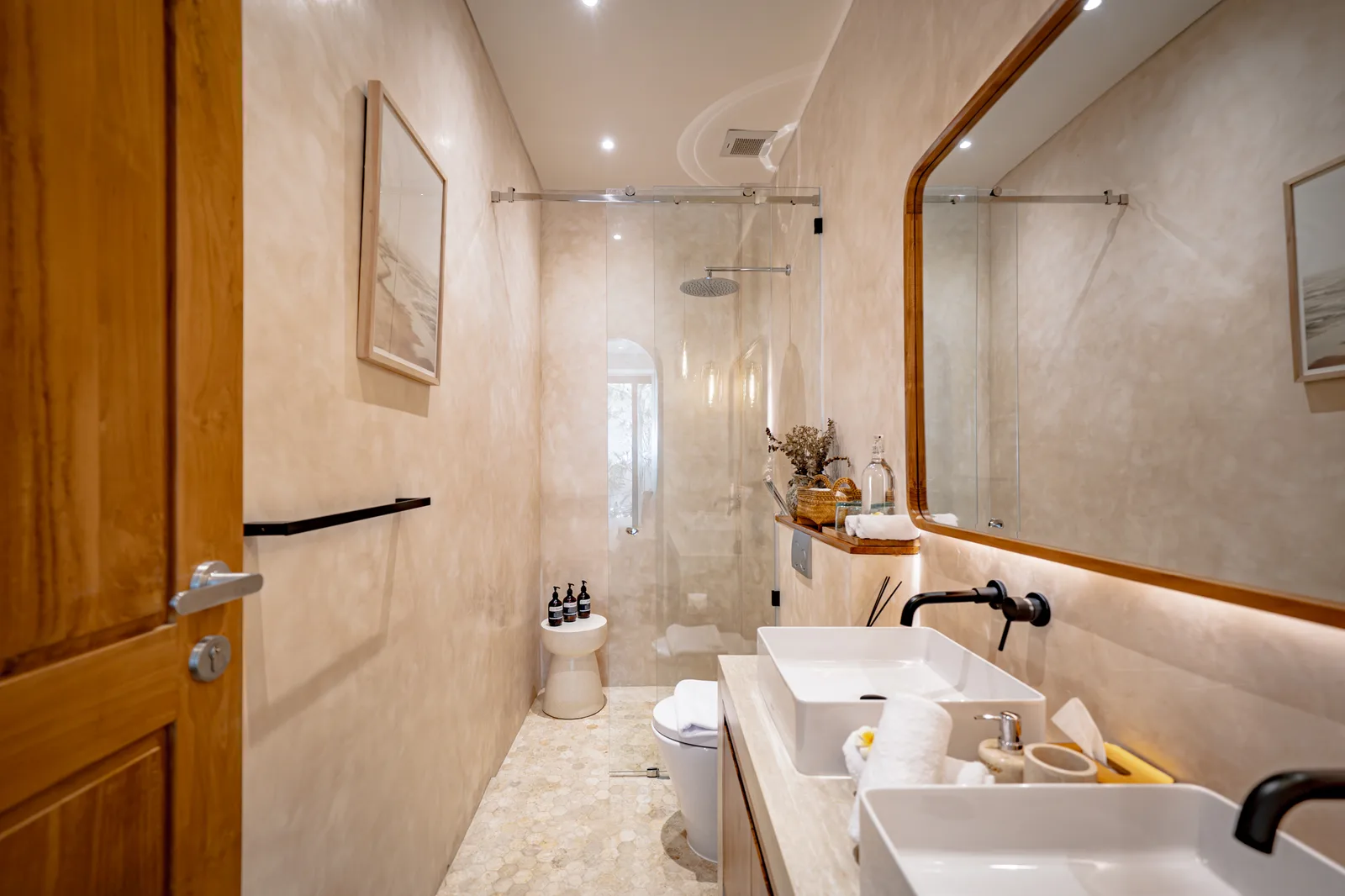 Un baño luminoso con azulejos cuenta con una ducha acristalada, un largo tocador con lavabos sobre encimera y un gran espejo.