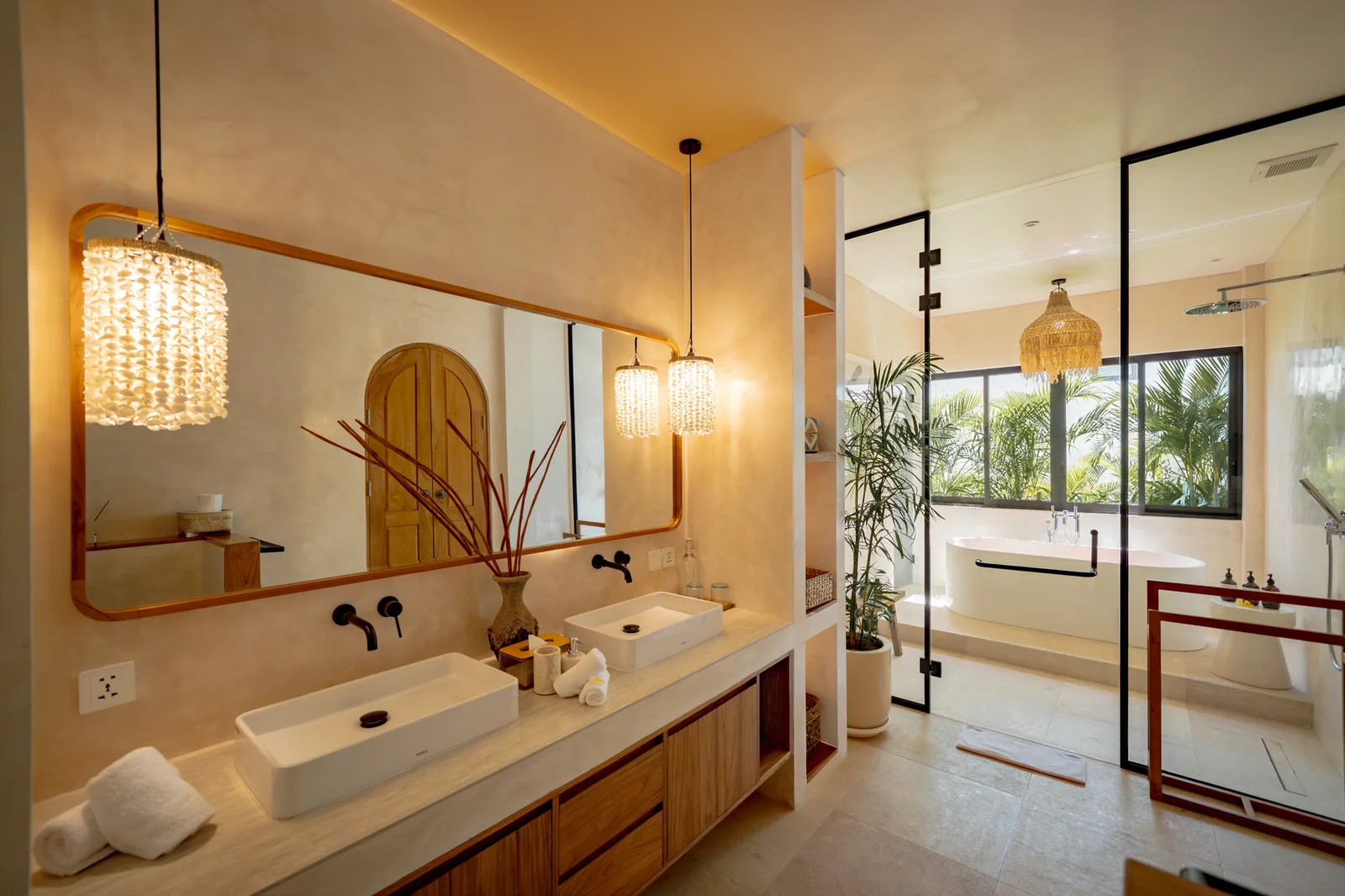 Un baño luminoso cuenta con dos lavabos sobre encimera, un espejo largo, luces colgantes cálidas y una bañera con mampara de vidrio.
