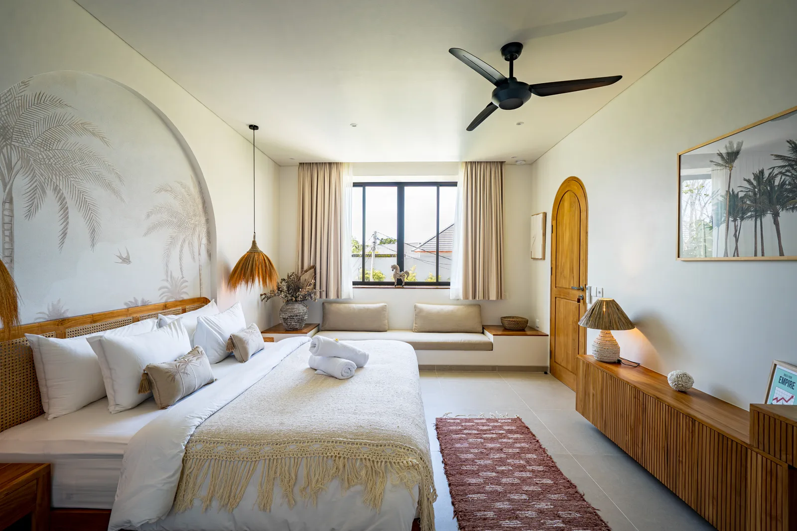 Un dormitorio luminoso tiene una gran cama blanca, un rincón de asiento junto a la ventana y un largo mueble de madera.