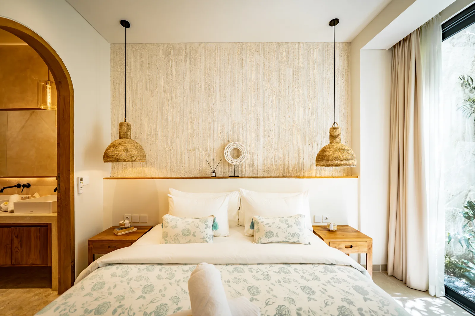 Un dormitorio con una cama bien tendida, ropa de cama estampada, mesitas de noche y lámparas colgantes a juego.