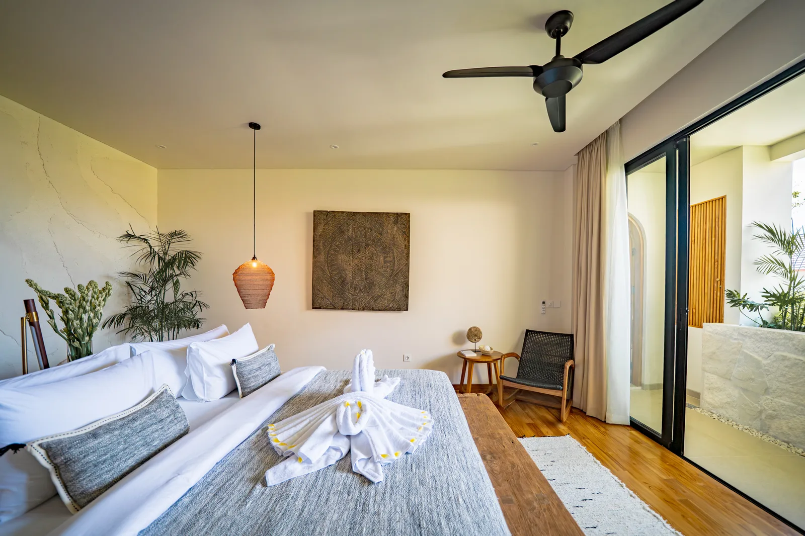 Un dormitorio luminoso cuenta con una cama bien arreglada, asientos junto a la cama, un ventilador de techo y puertas corredizas de vidrio.