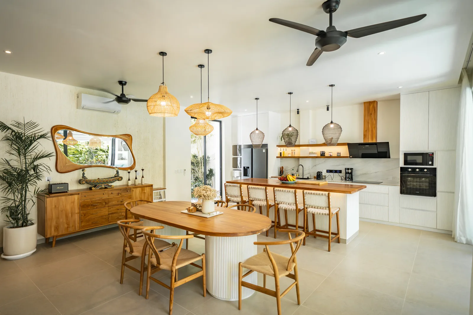 Una luminosa cocina-comedor de planta abierta cuenta con una mesa de madera, lámparas colgantes tejidas y un ventilador de techo.