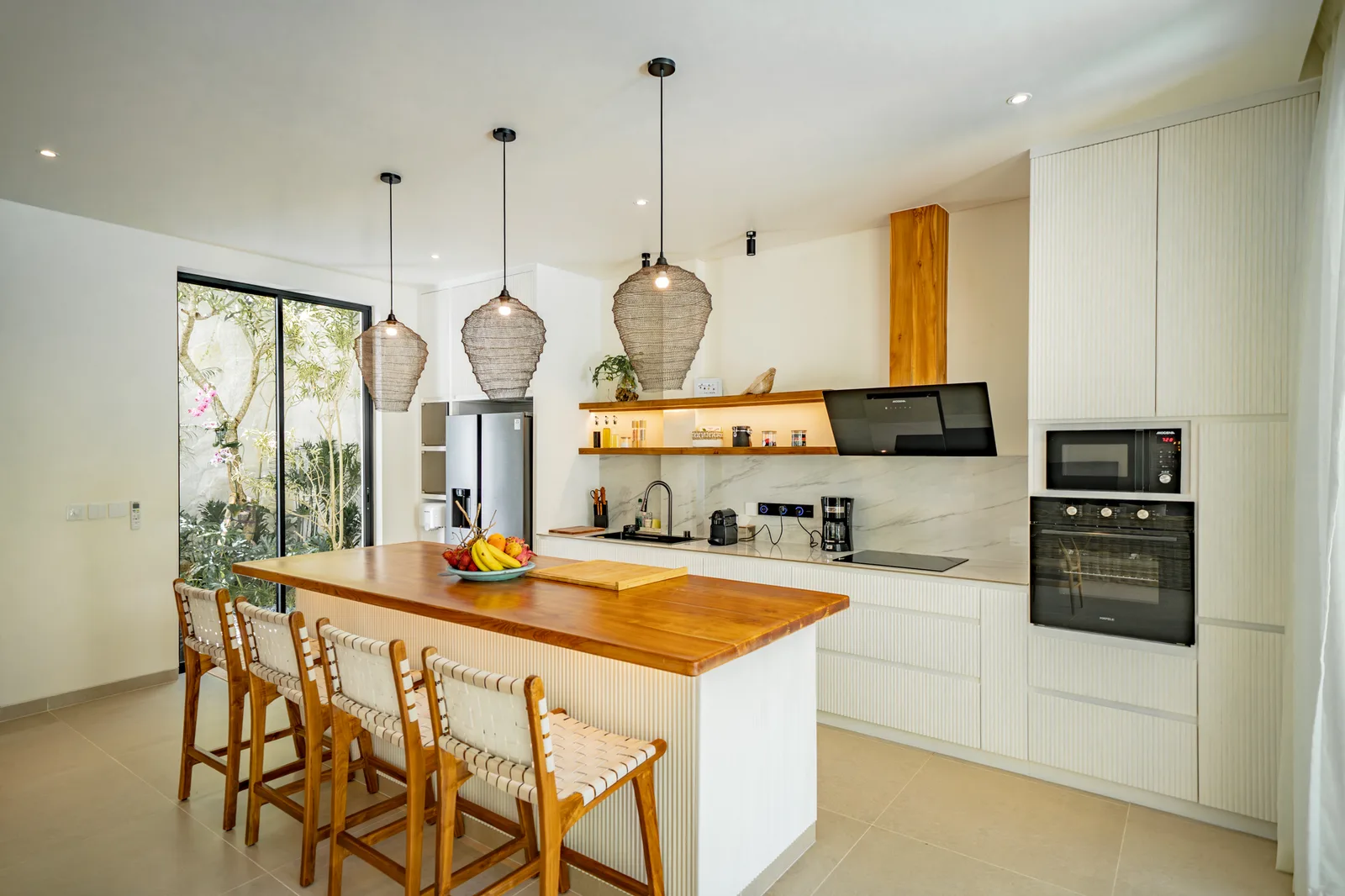 Una cocina moderna y luminosa cuenta con una isla de madera con taburetes, lámparas colgantes y electrodomésticos integrados.