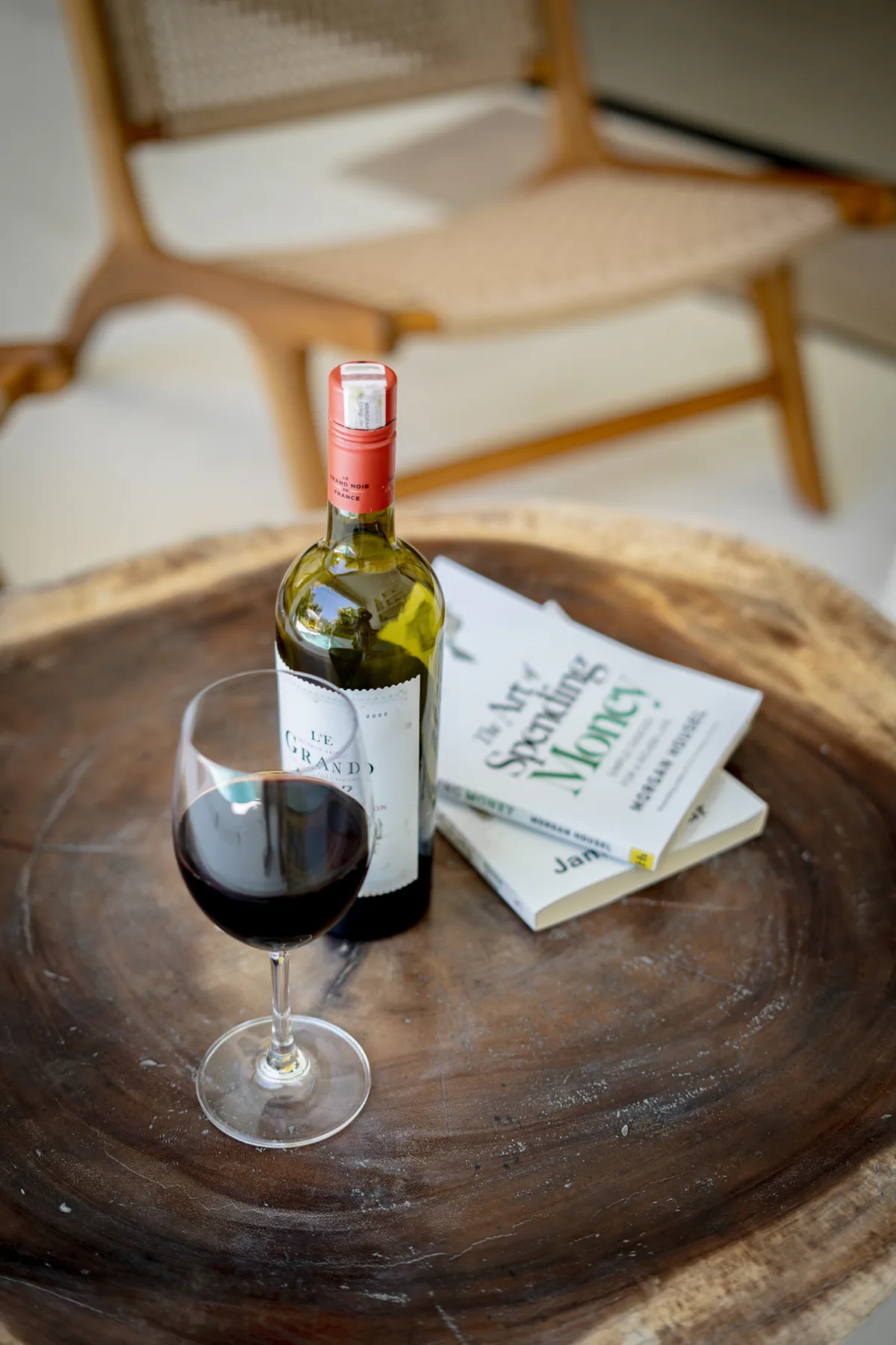 Una botella de vino tinto, una copa servida y un libro descansan sobre una mesa redonda de madera.