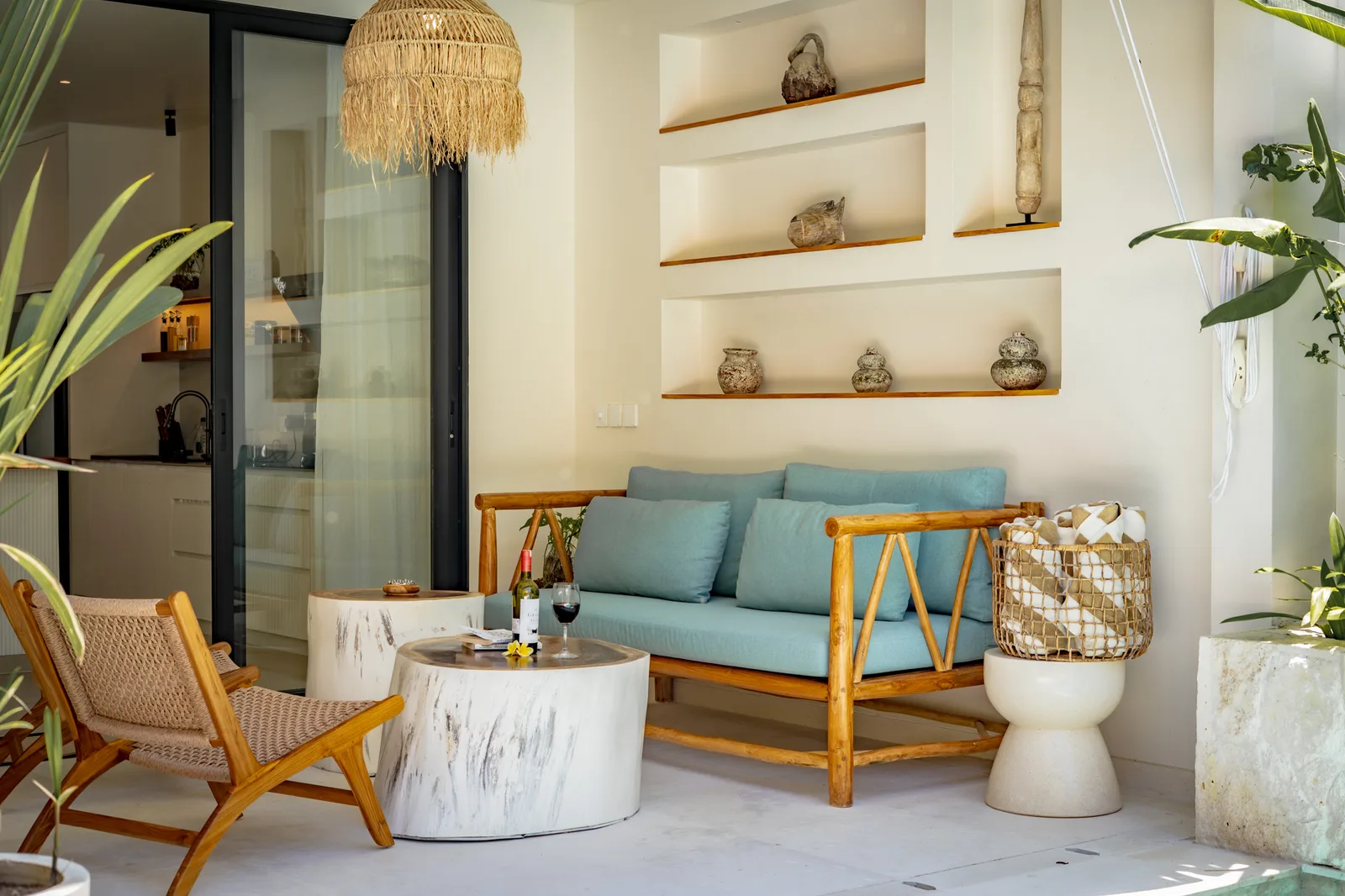 Una sala luminosa con sofá azul, sillón tejido, mesa de centro redonda y estantes empotrados.
