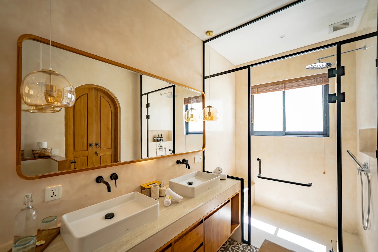 Un tocador de baño con dos lavabos sobre encimera y un espejo grande frente a una ducha con mampara de vidrio.
