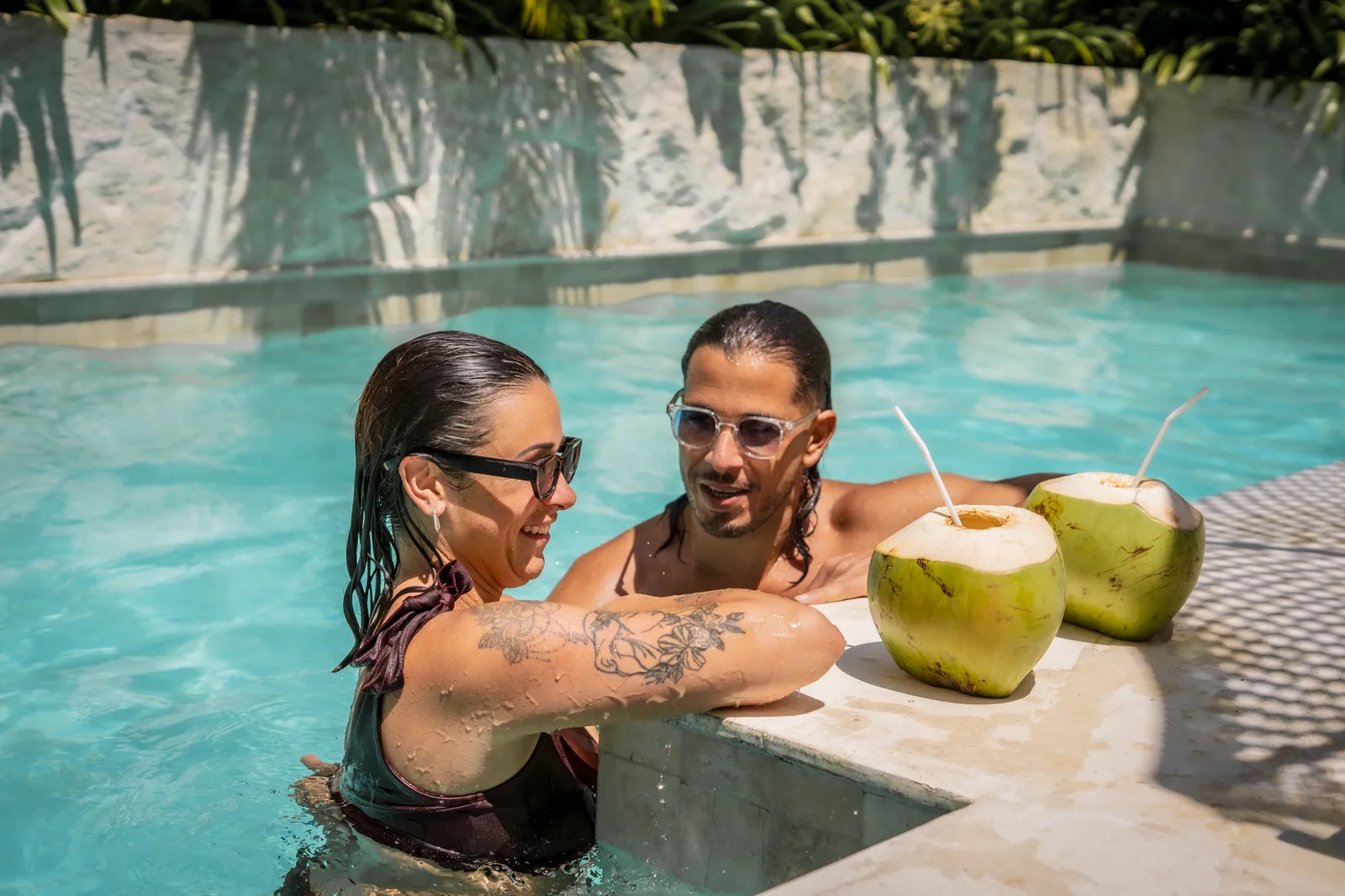 Dos personas descansan en una piscina junto a un borde con dos cocos.