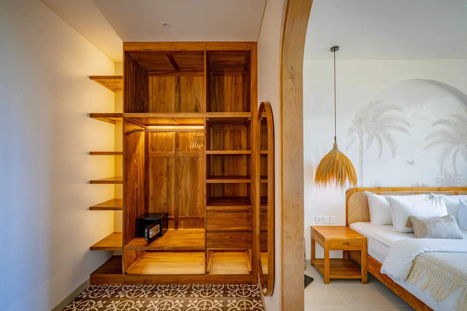 Una estantería y un armario de madera junto a un dormitorio con cama blanca y lámpara colgante.