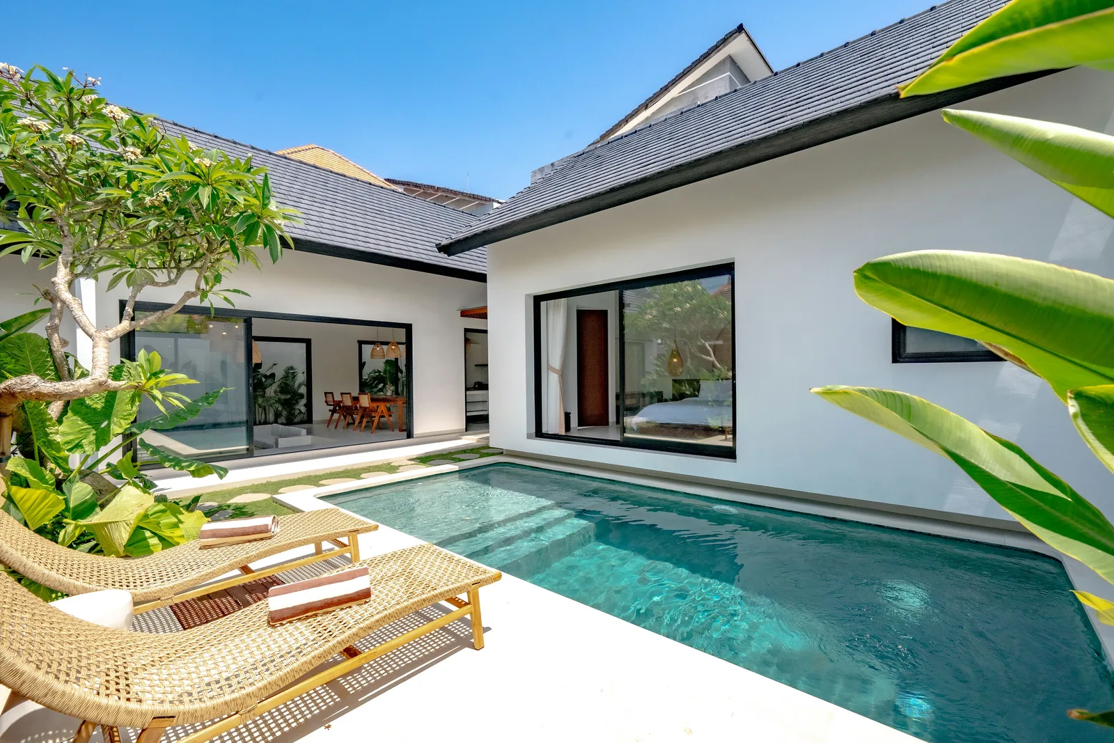 A courtyard pool sits beside a white house with sliding glass doors and outdoor seating.