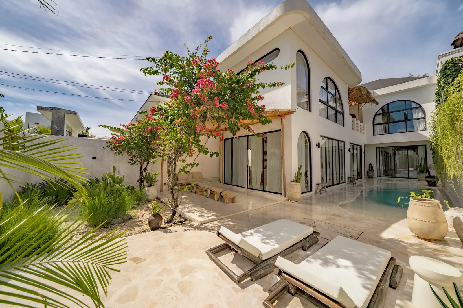 A modern white house surrounds a courtyard with a pool and lounge seating.