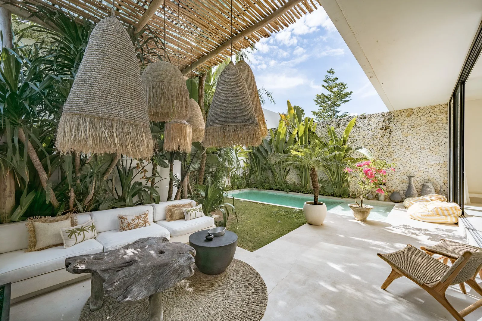 Un patio tropical al aire libre con asientos, lámparas colgantes tejidas y una pequeña piscina.