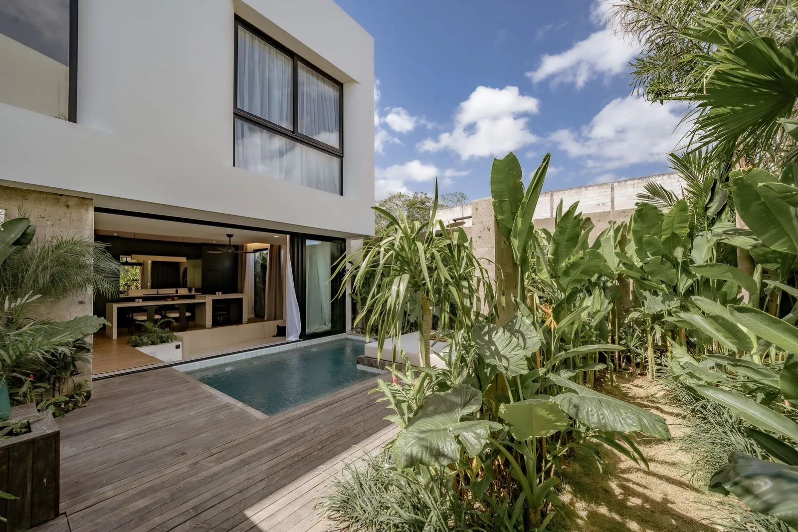 Una casa moderna se abre a una pequeña piscina junto a un frondoso jardín tropical.
