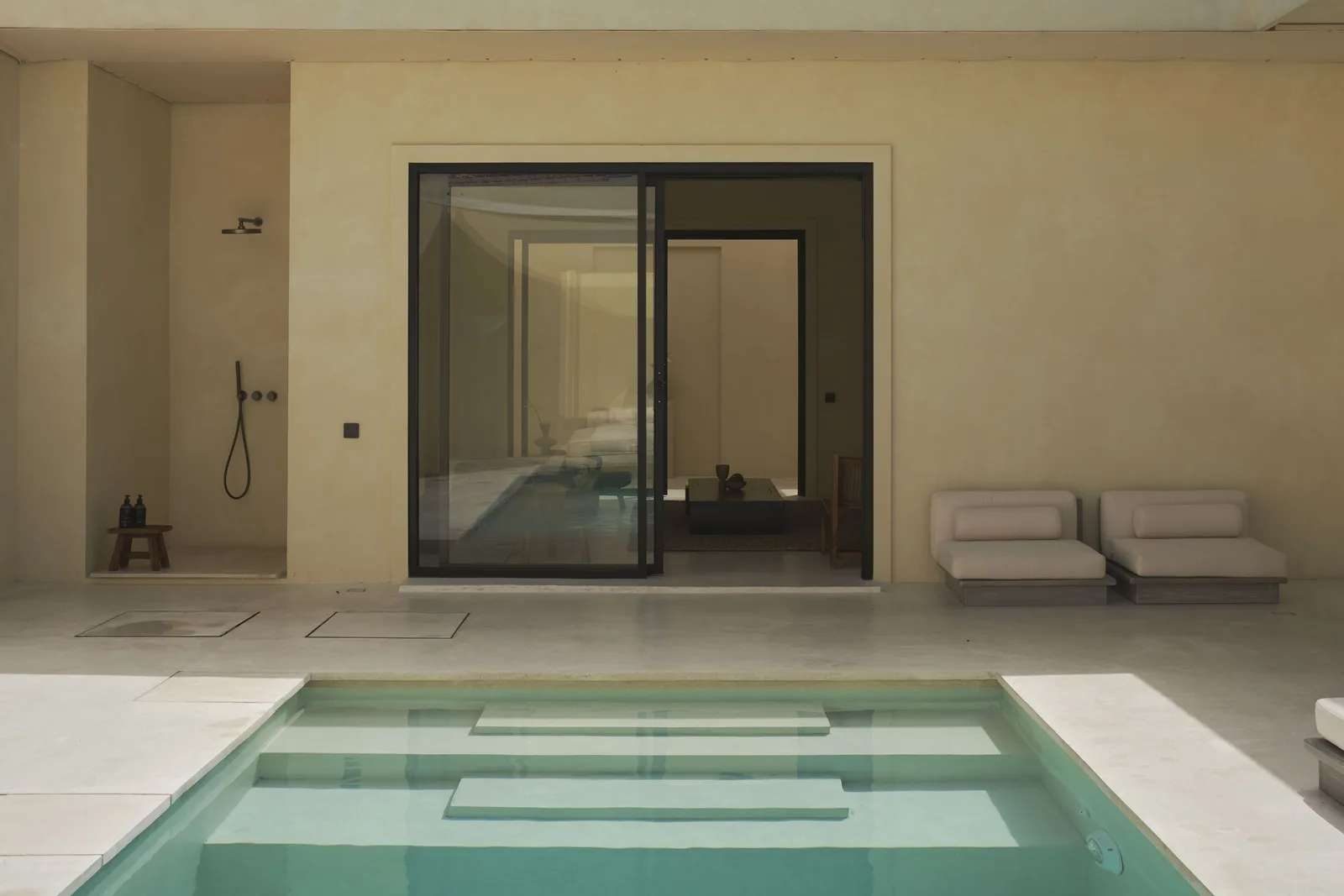 A swimming pool sits beside a glass door and an outdoor shower.