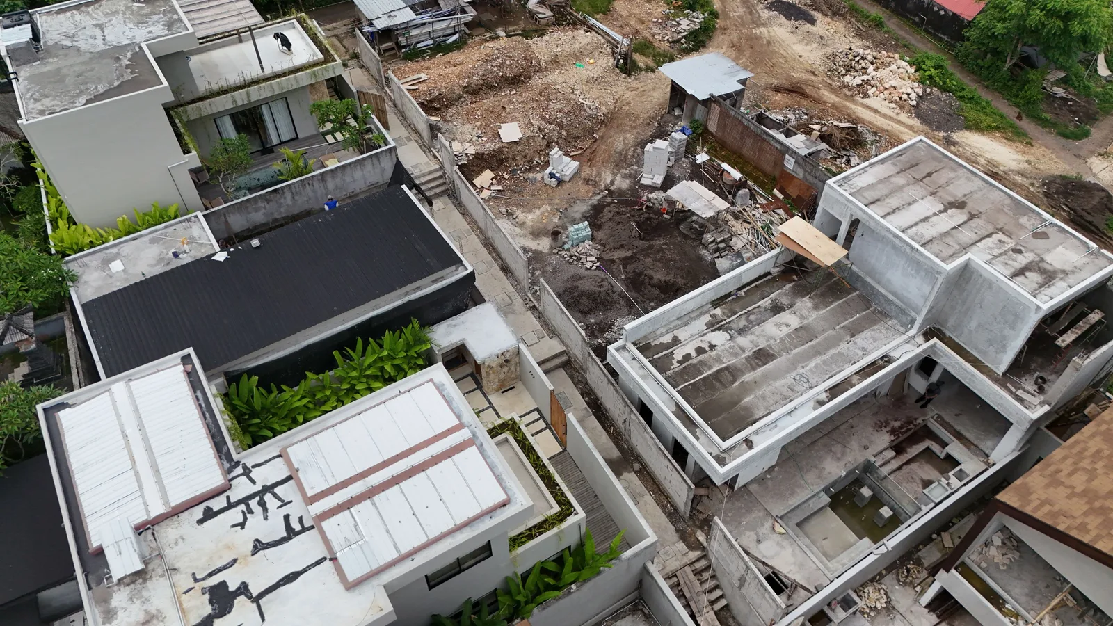 An aerial view shows modern concrete buildings beside an unfinished construction site with scattered debris.