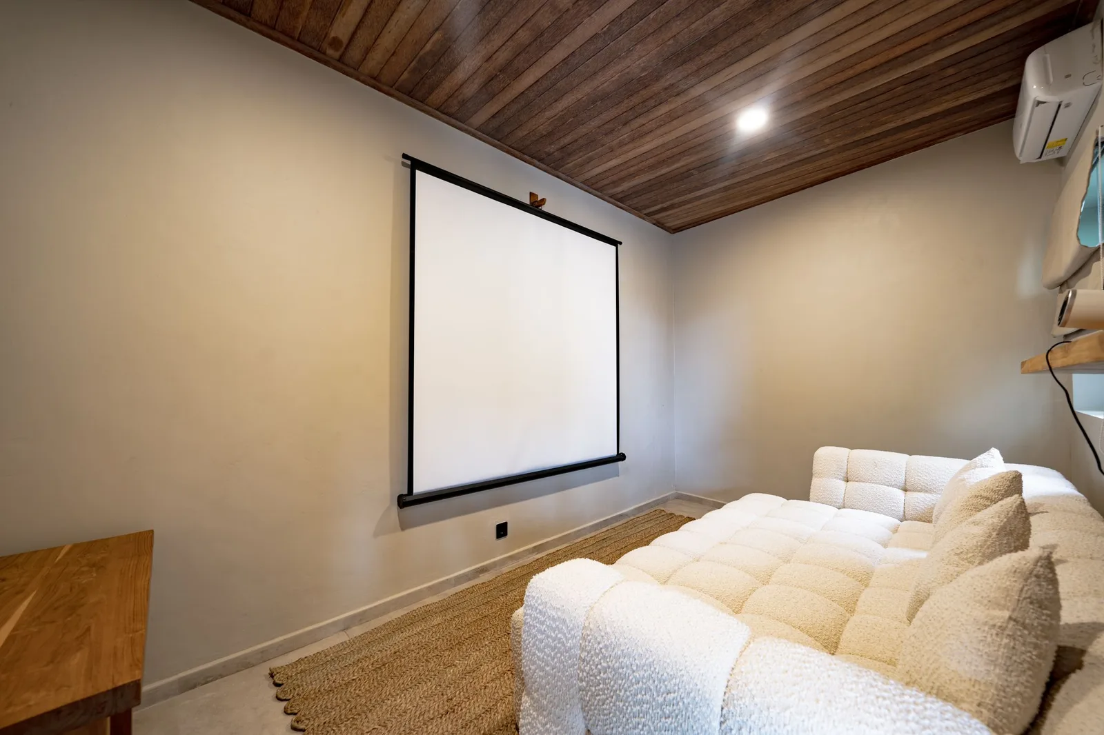 A cozy media room has a large projection screen, cushioned white seating, and a wood-paneled ceiling.