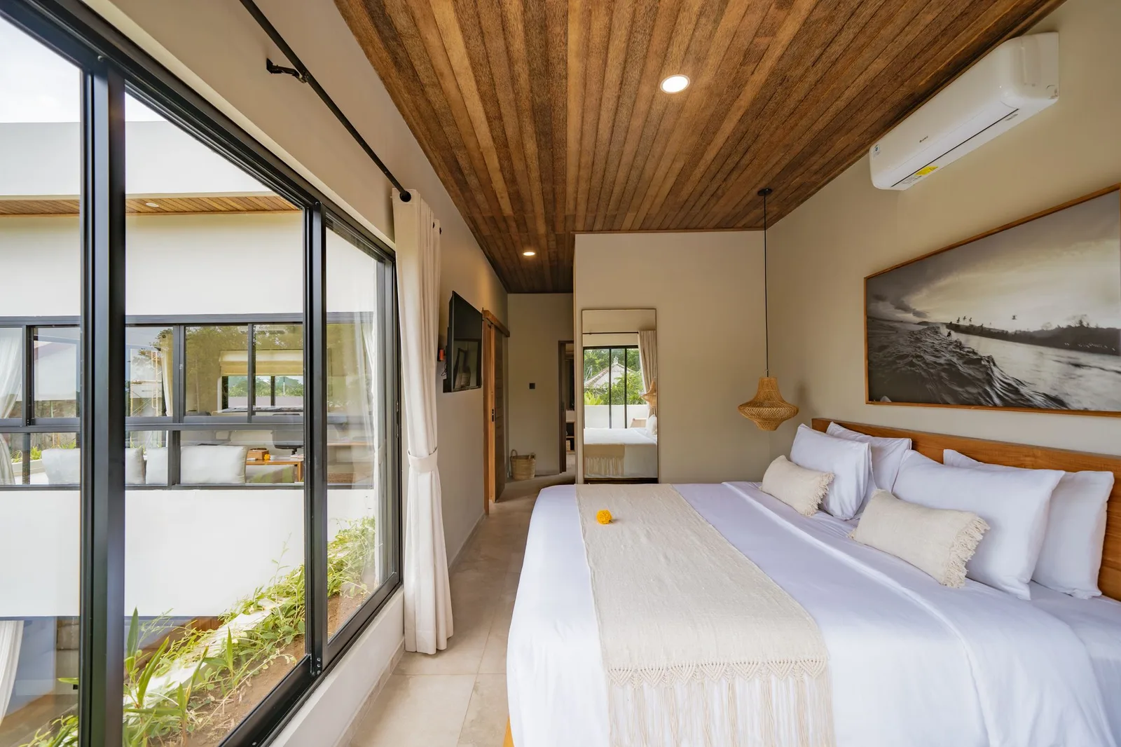 A bright bedroom with a king-size bed, glass sliding doors, and a wood-paneled ceiling.