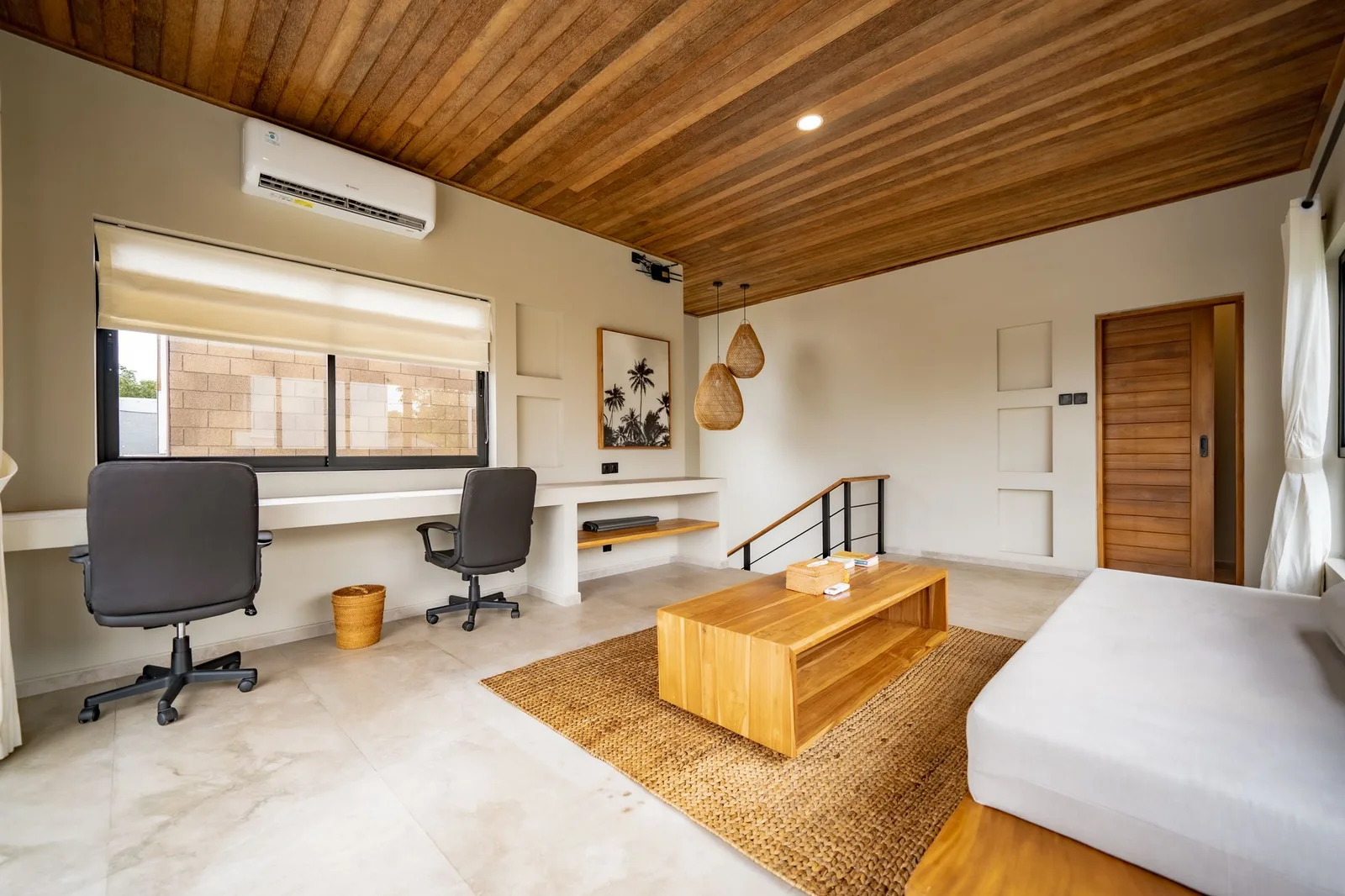 A bright room with a wooden ceiling, two desk chairs, a low table, and a bed.