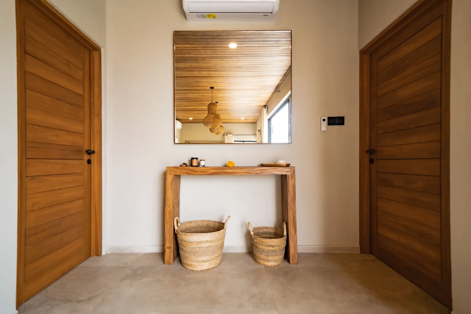 A hallway with wooden doors, a console table, woven baskets, and a large wall mirror.