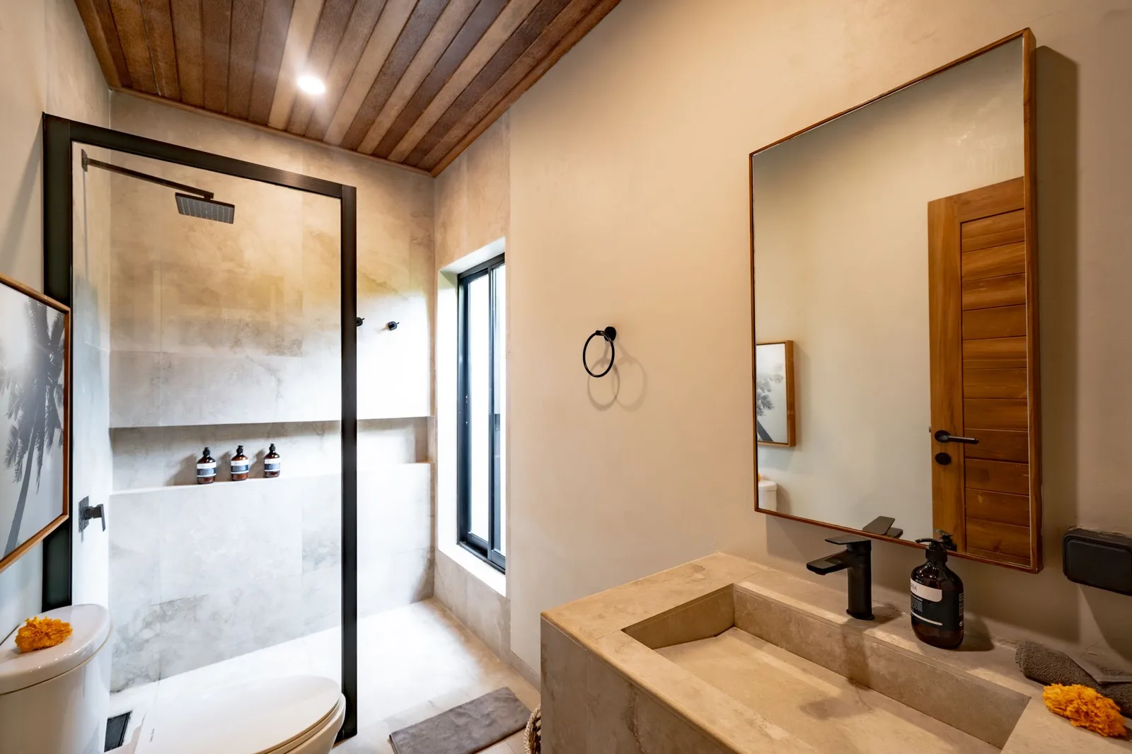 A modern bathroom with a glass shower, stone sink counter, large mirror, and wooden ceiling.