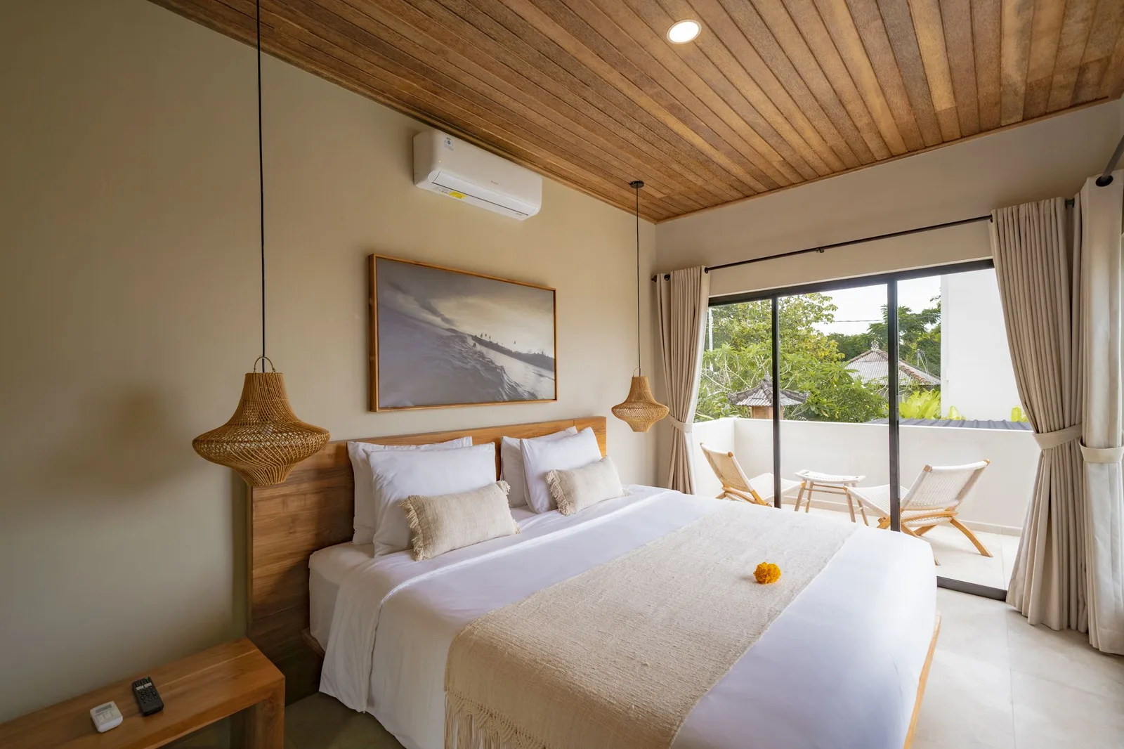 A bedroom with a white bed, wood-paneled ceiling, and sliding glass doors opening onto a balcony.