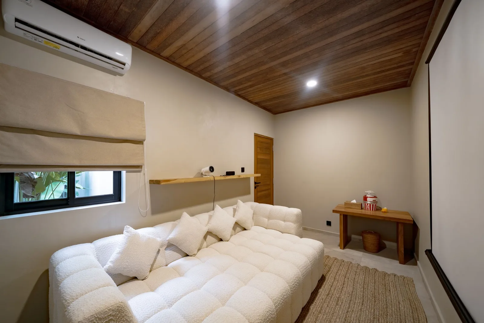 A bedroom with a large white bed, a wooden ceiling, a small desk, and a shaded window.