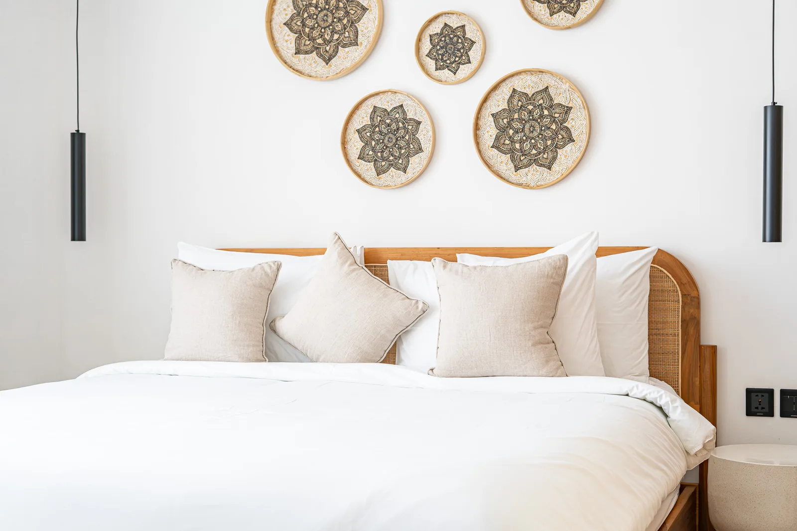A bright bedroom features a white bed, woven wooden headboard, and circular decorative wall pieces.