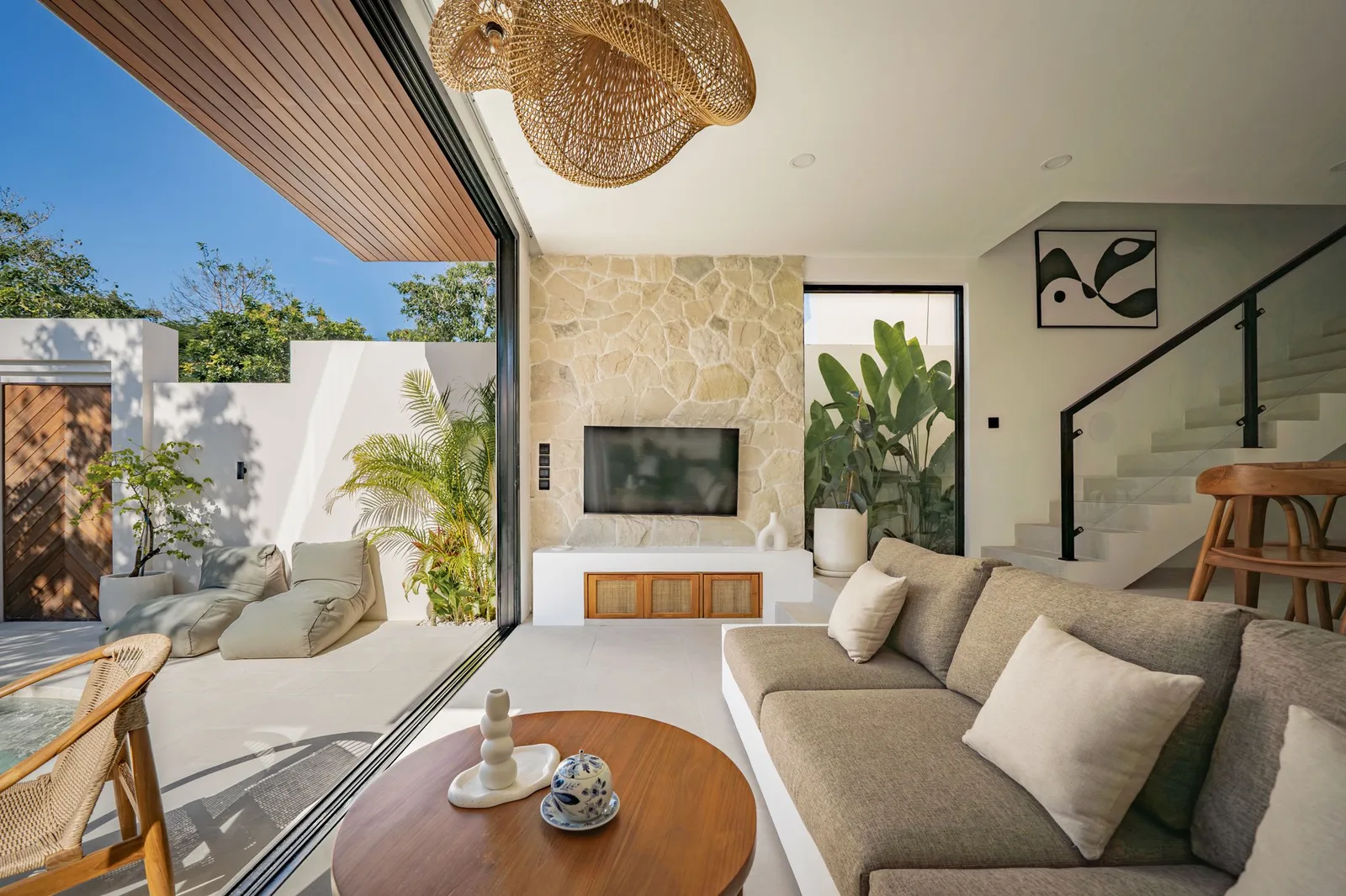 A bright living room opens onto a patio, with a large sofa, stone fireplace, and round coffee table.