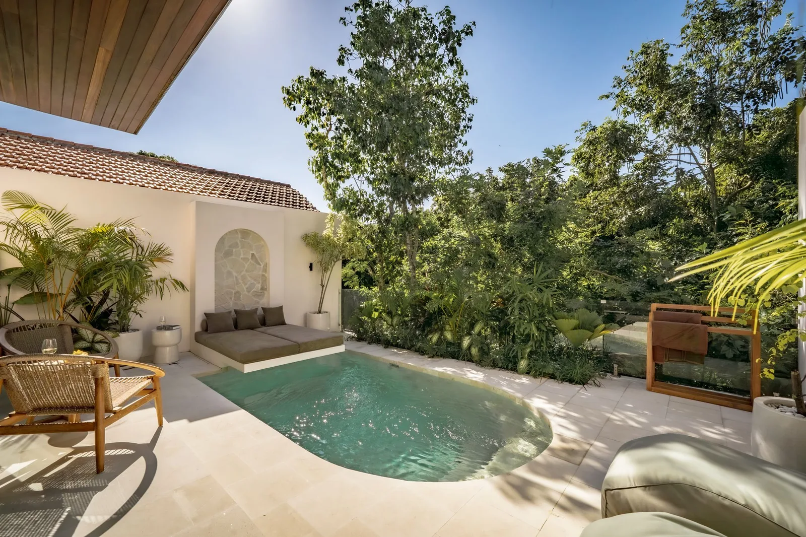 A small outdoor pool sits beside a tiled-roof building, with lounge seating and dense tropical greenery.