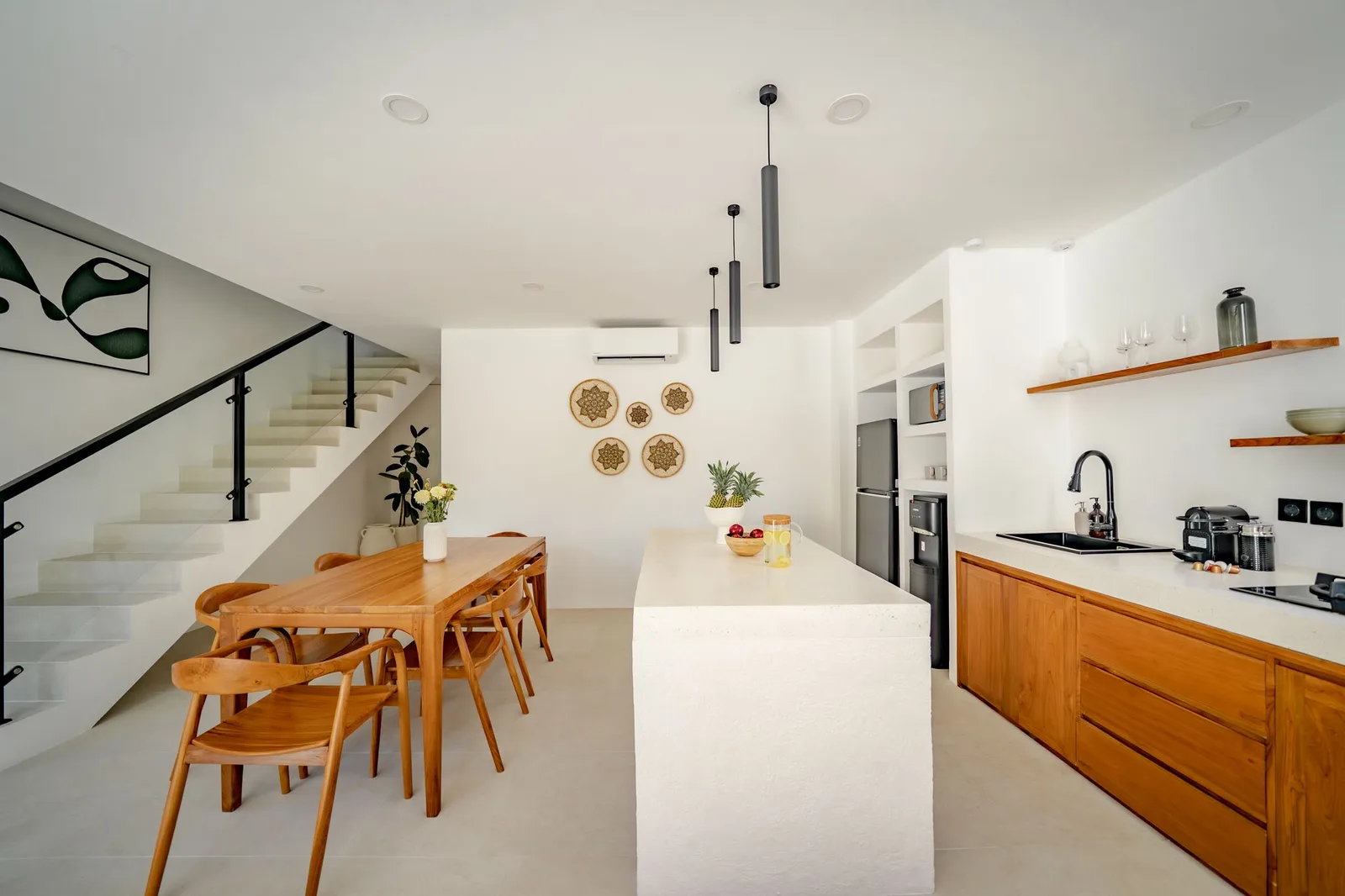 A bright open-plan kitchen and dining area features a long island, wooden cabinets, and a staircase.