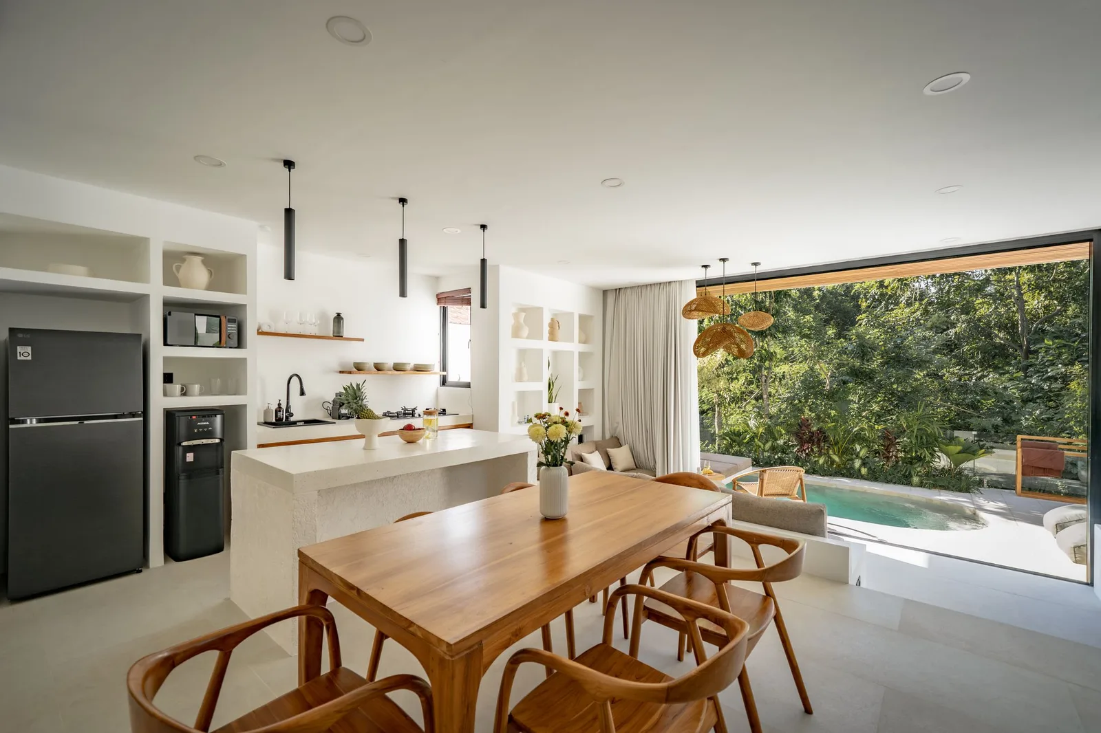 An open-plan kitchen and dining area features a wooden table, a stone island, and glass doors overlooking a pool.