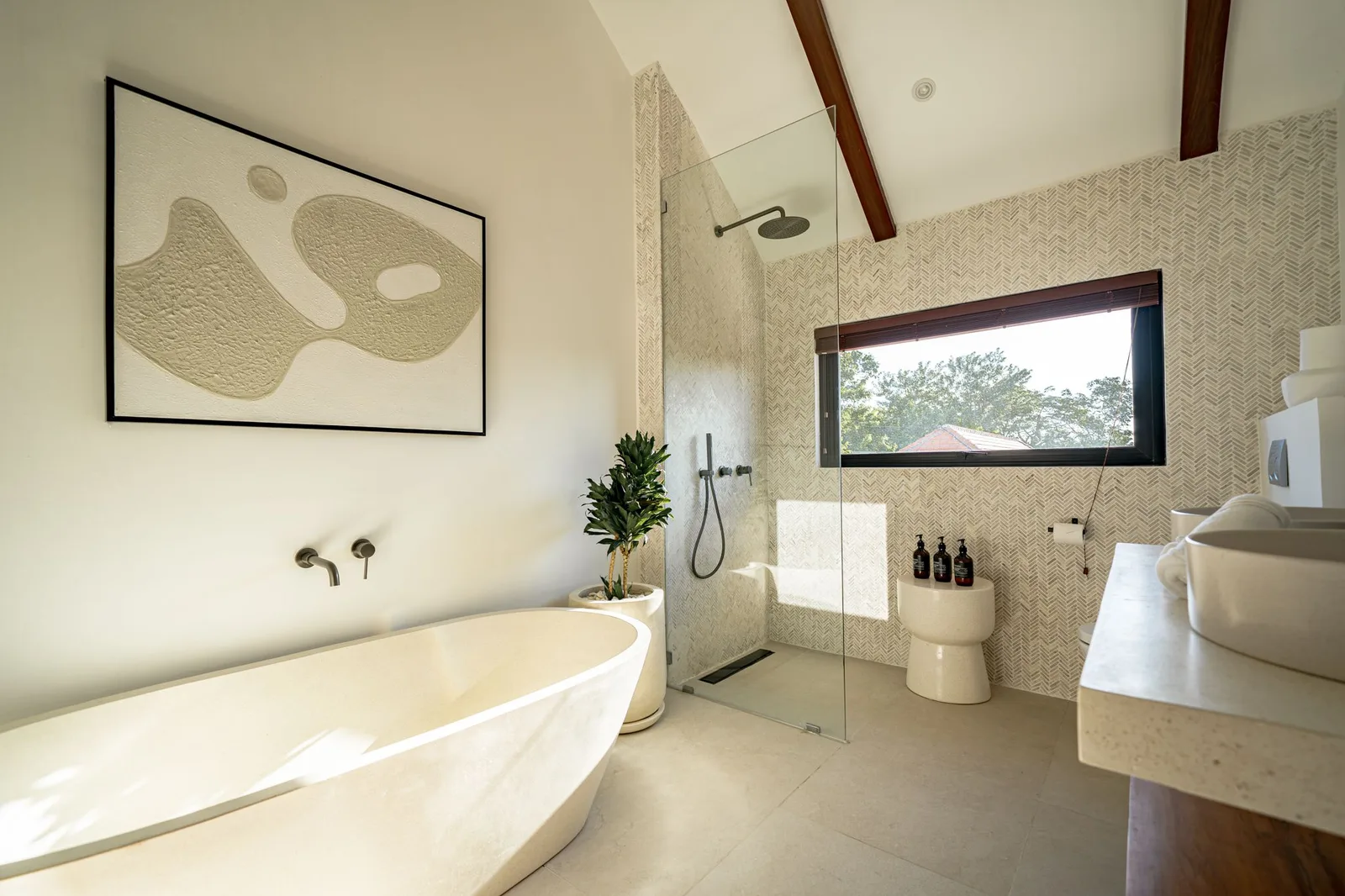 A bright bathroom features a freestanding bathtub, glass shower, toilet, and a wide window.