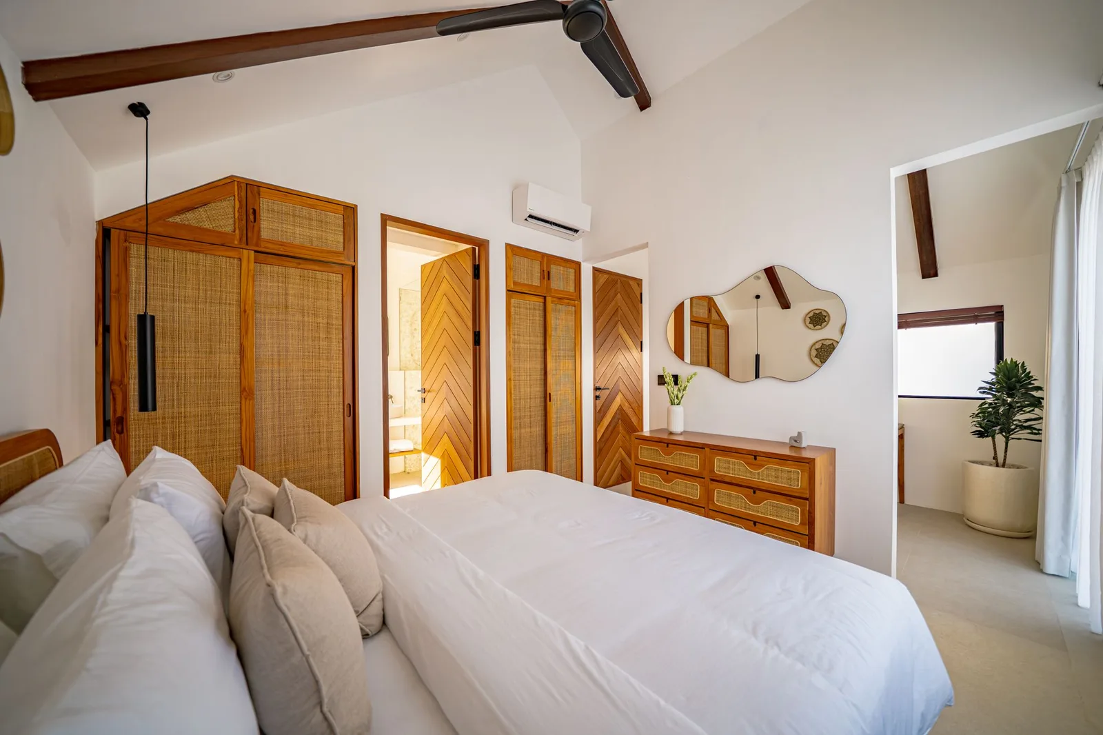 A bright bedroom with a white bed, woven wooden wardrobes, a dresser, and a wall mirror.