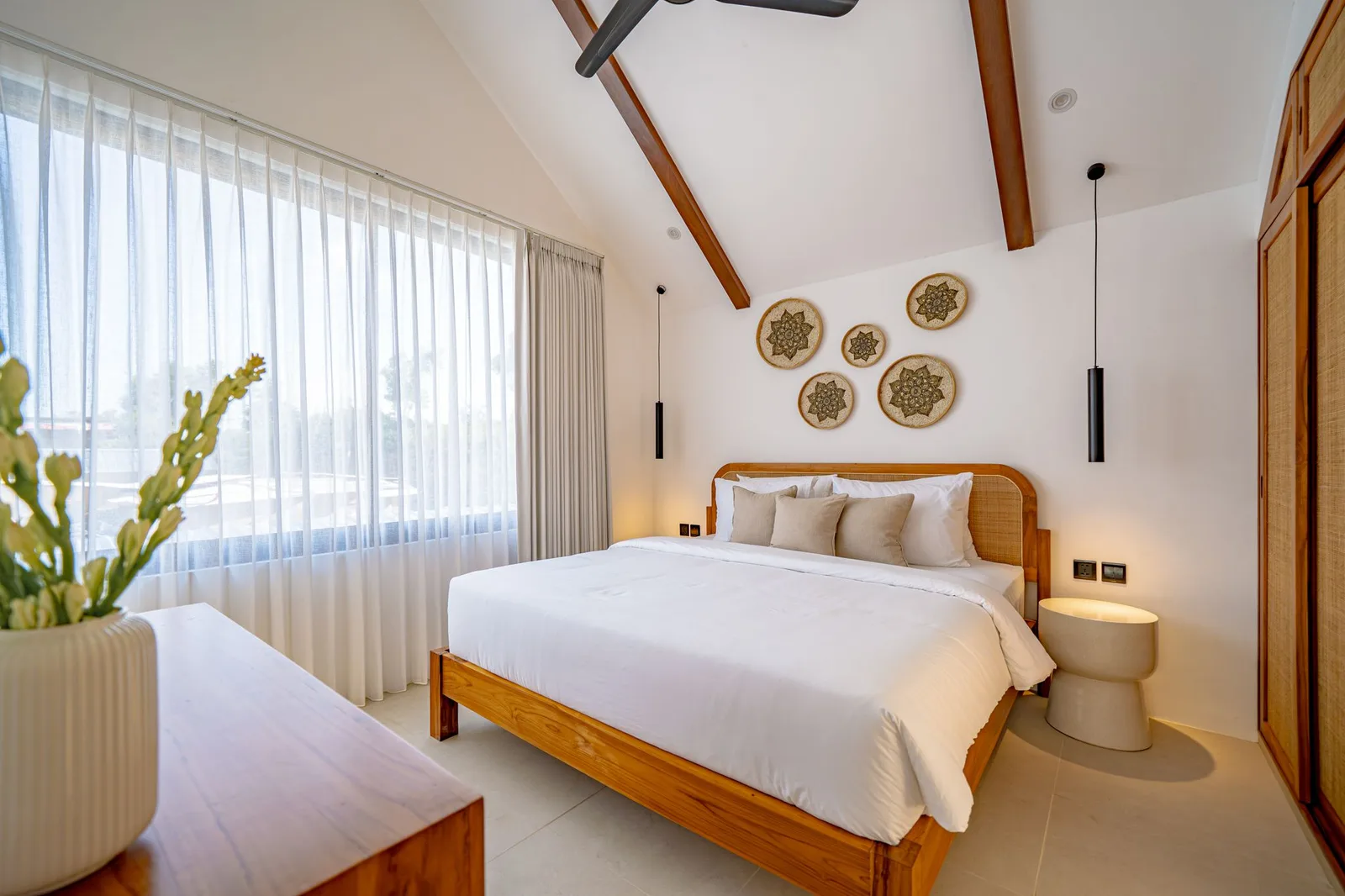 Bedroom with a wooden bed, white bedding, decorative wall plates, and a large curtained window.