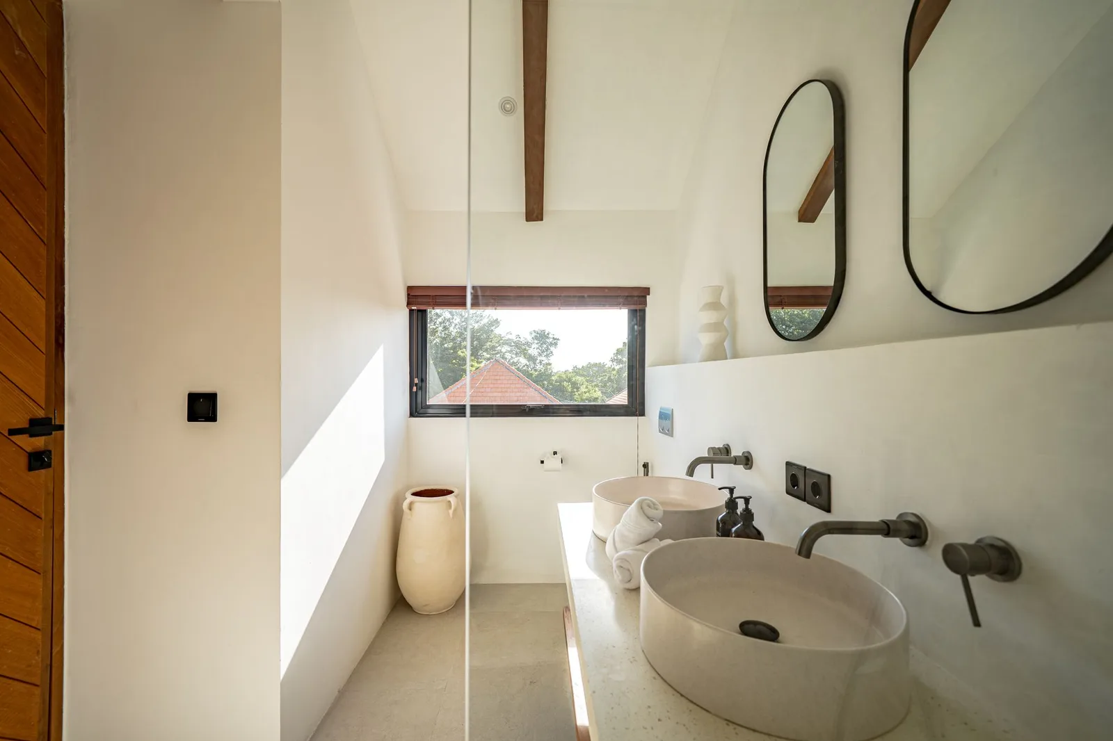 A bright bathroom has a walk-in shower, a freestanding tub, and a large vessel sink beneath wall mirrors.