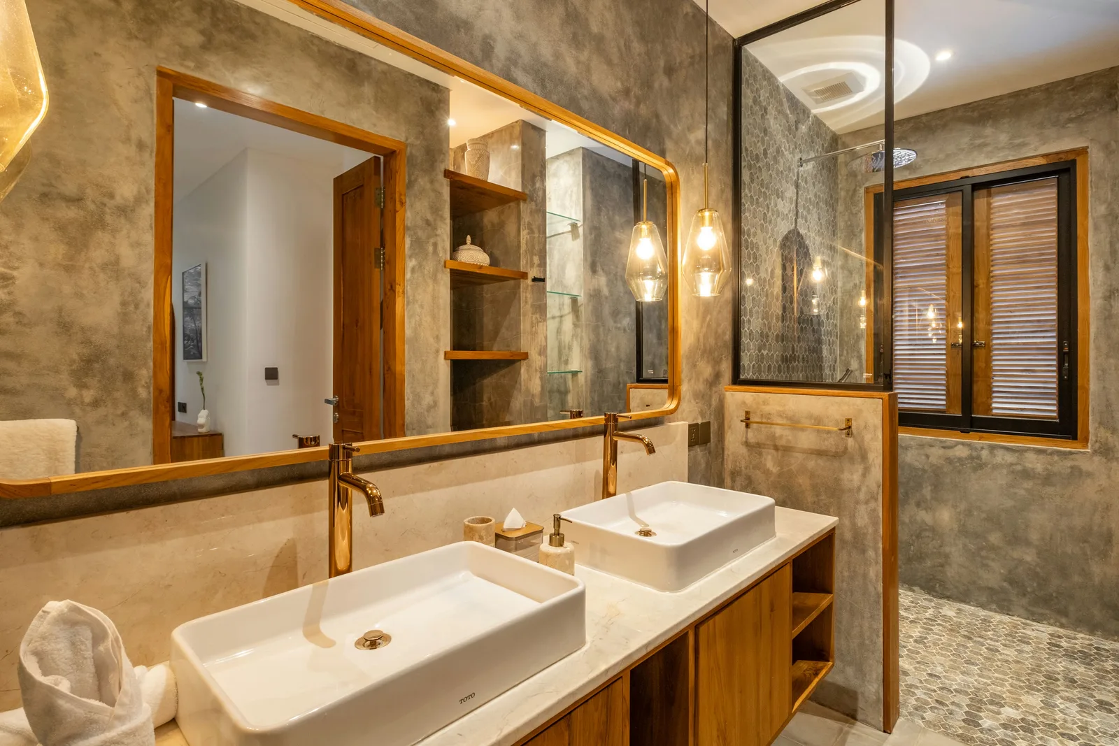 Un baño moderno tiene dos lavabos blancos sobre encimera, muebles de madera, espejos grandes y una ventana con persianas.
