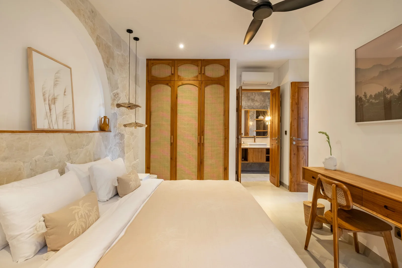 Un dormitorio luminoso con una cama grande, un armario de paneles tejidos y un escritorio de madera bajo un ventilador de techo.