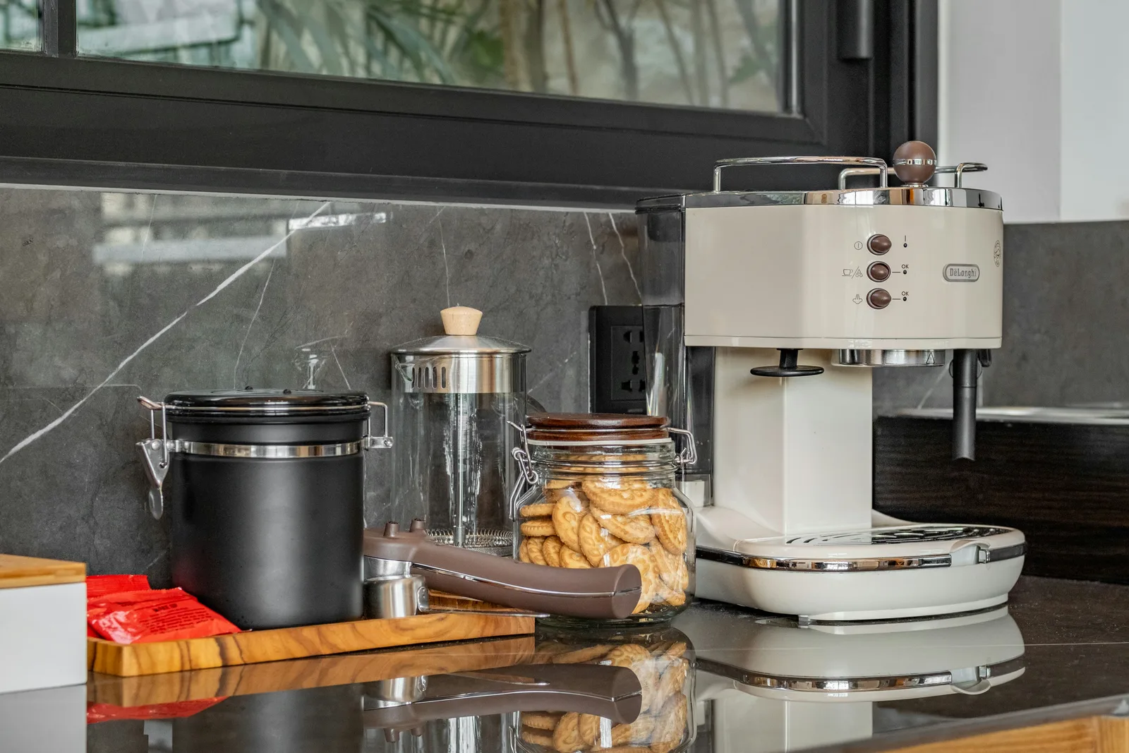Una encimera de cocina tiene una cafetera espresso blanca, una olla negra y frascos de café y galletas.