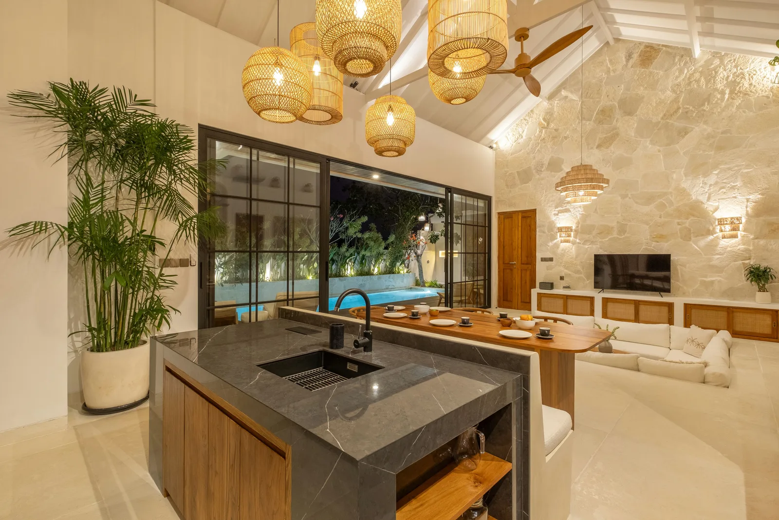 Una cocina y sala de estar diáfanas cuentan con una isla de piedra oscura, mesa de comedor y vistas a la piscina.