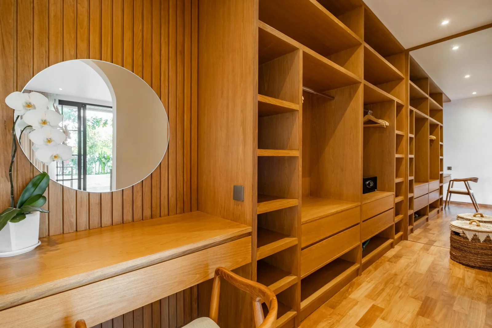 Un vestidor revestido de madera tiene estantes hasta el techo, cajones, un espejo redondo y un taburete.